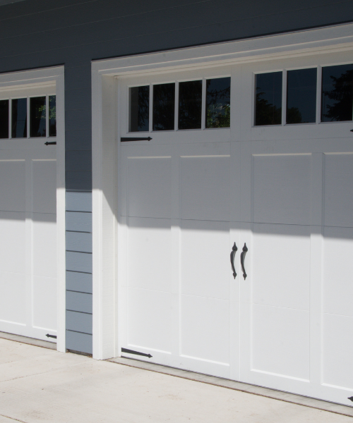White garage doors with decorative windows on a modern residential home, representing Pride Garage Doors' craftsmanship