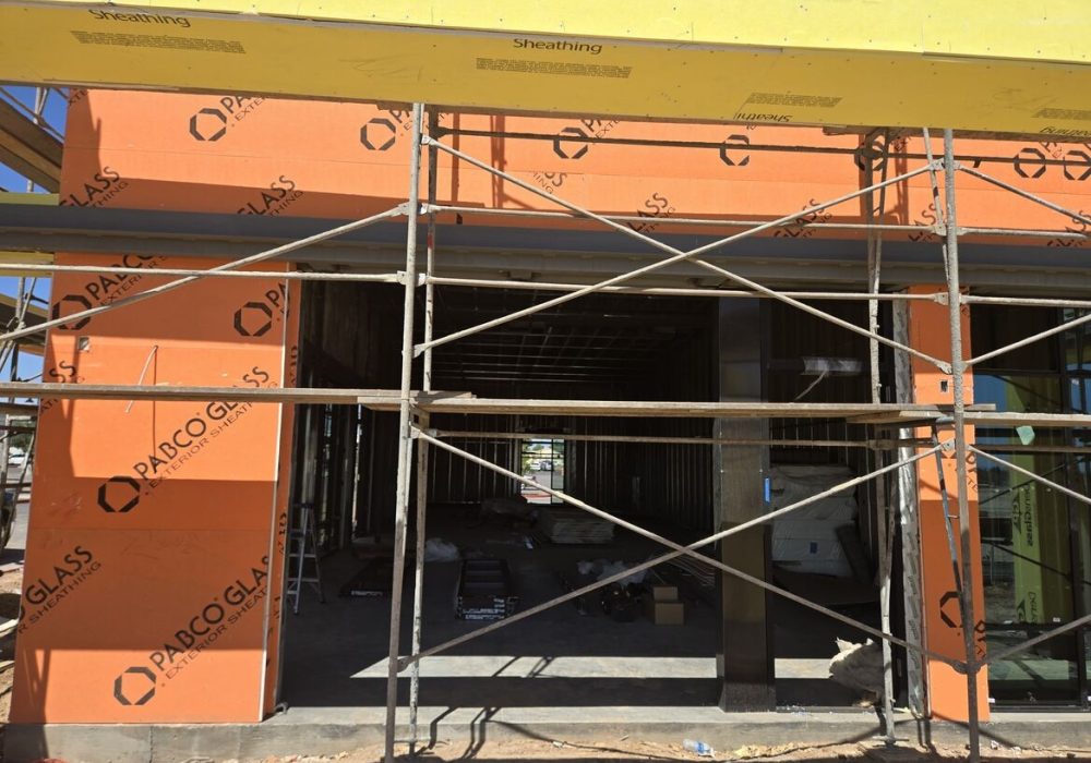 Construction site showing a partially finished building with orange sheathing, yellow scaffolding, and open framing.